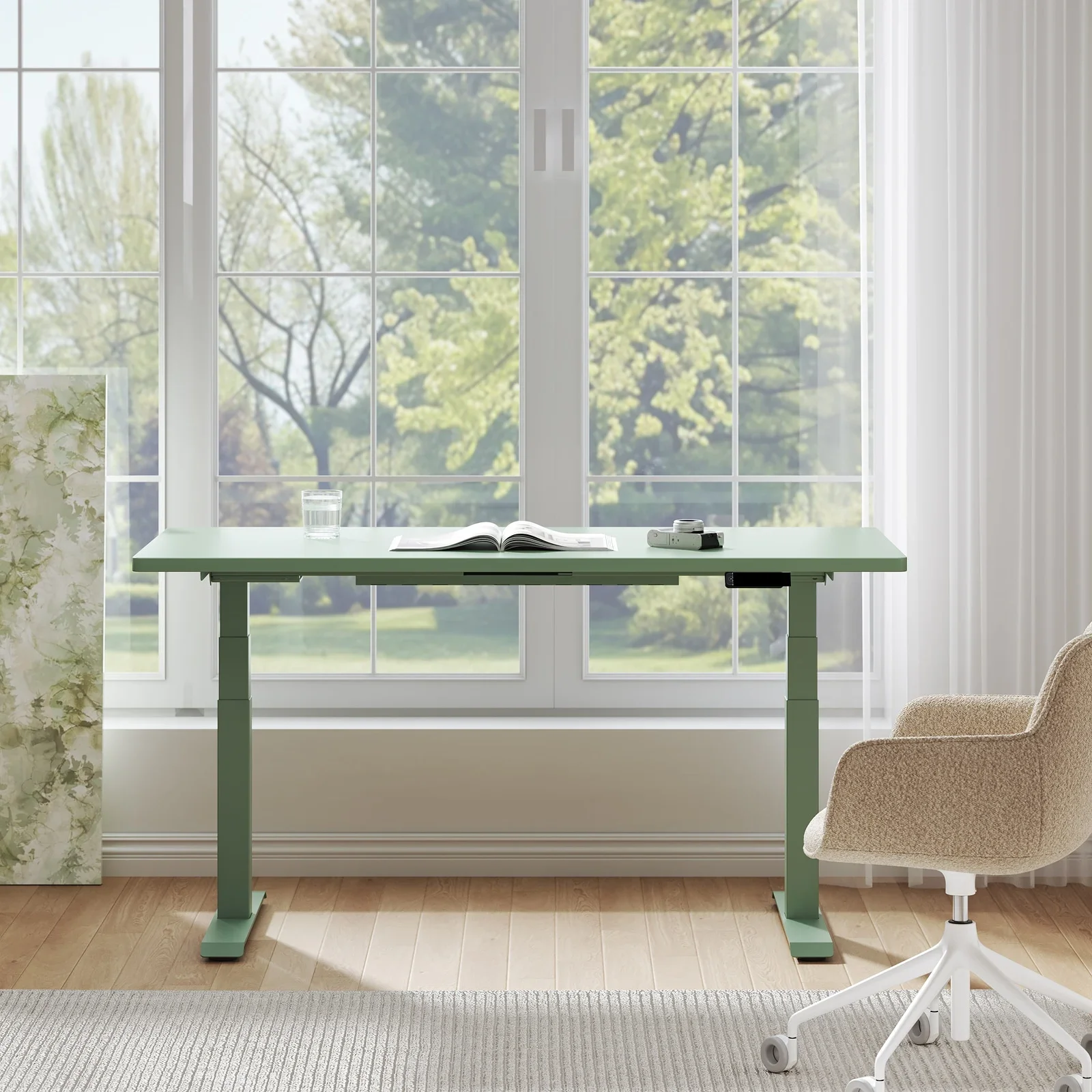Sage-green frame and top desk by a large window with a boucle chair and garden view.